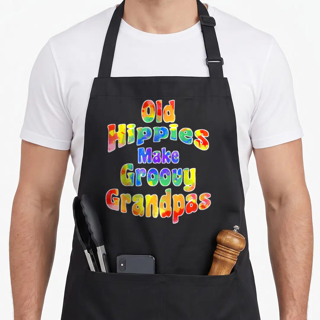 Hippy lady groovy apron - Colorful stacked text reading Old Hippies Make Groovy Grandpas on black fabric — shown on a black cotton canvas apron against a white background