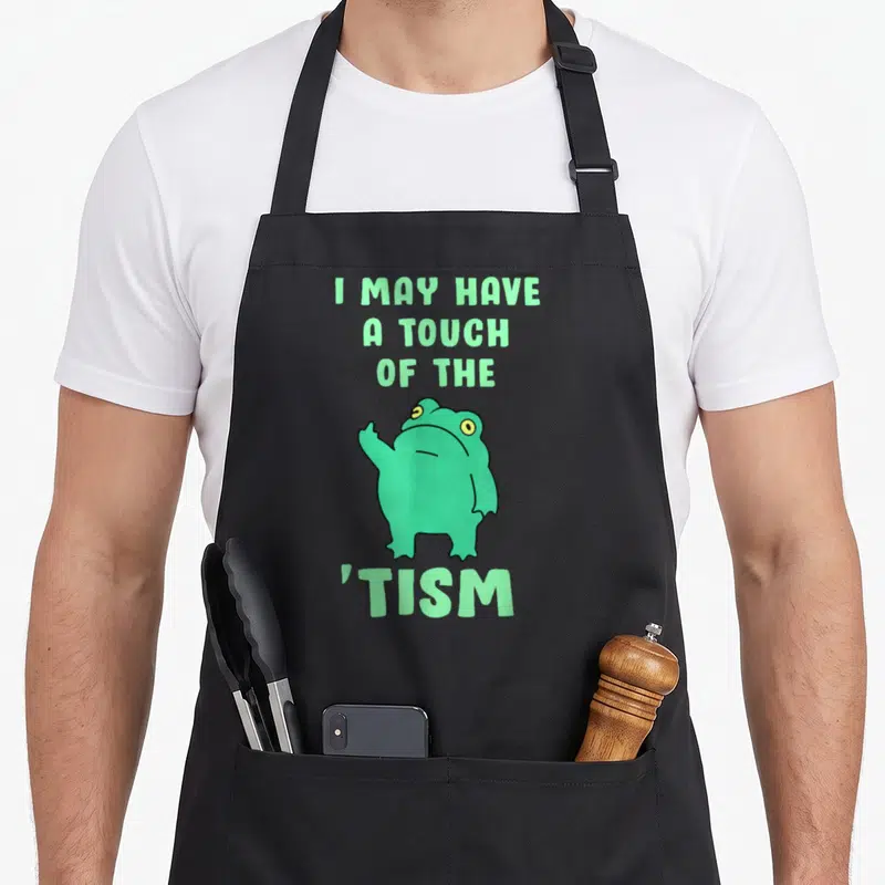 May frog aprons - Cartoon green frog pointing finger between light green text reading I MAY HAVE A TOUCH OF THE TISM — shown on a black cotton canvas apron against a white background