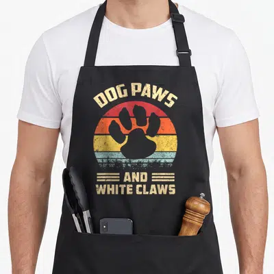 Claw dog apron - Retro striped sunset with grey paw print and DOG PAWS AND WHITE CLAWS text — shown on a black cotton canvas apron against a white background