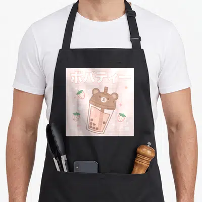 Bubble tea apron - Cartoon bear bubble tea cup on pink grid with Japanese text and strawberries — shown on a black cotton canvas apron against a white background