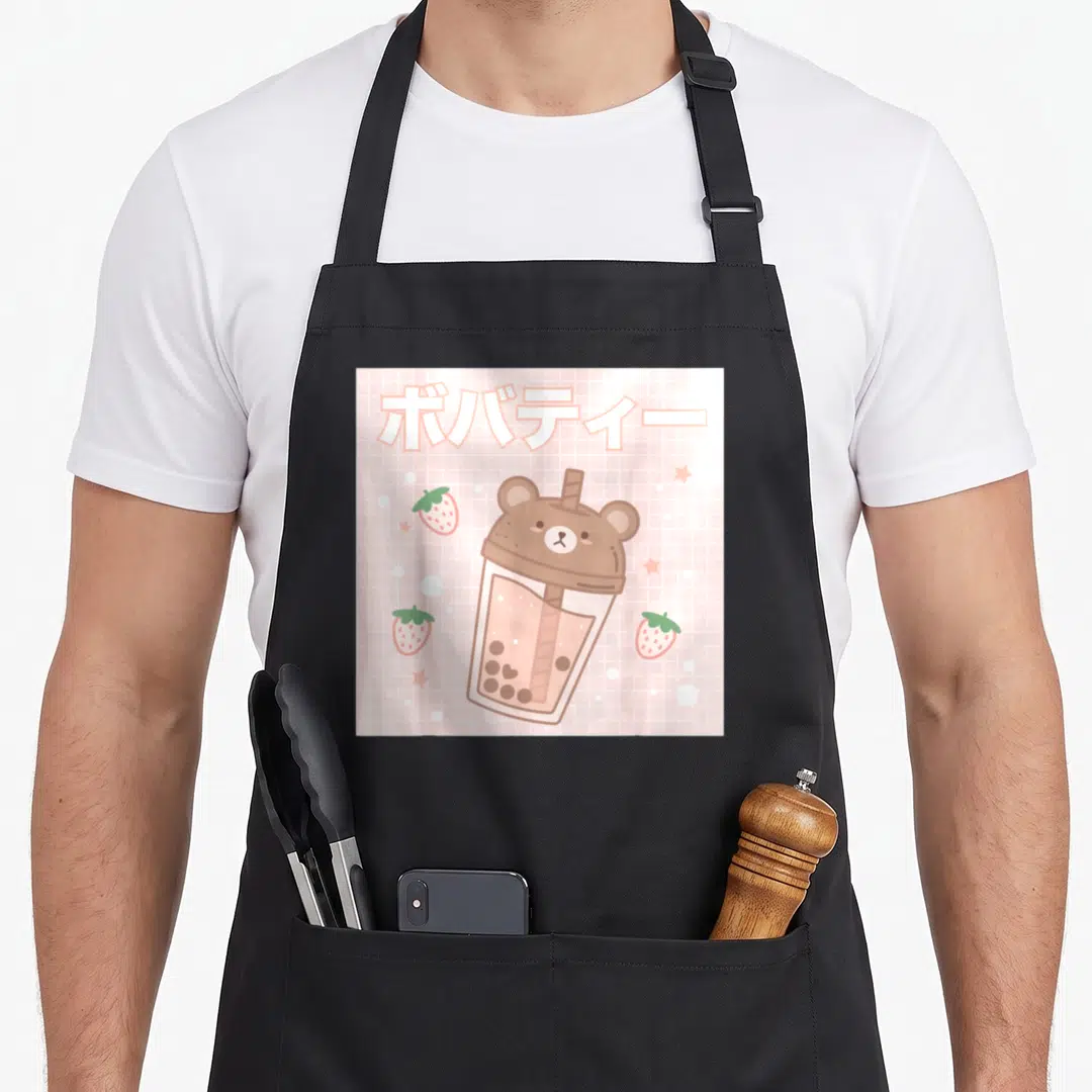Bubble tea apron - Cartoon bear bubble tea cup on pink grid with Japanese text and strawberries — shown on a black cotton canvas apron against a white background