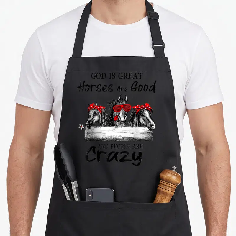 Funny god horse apron - Three horses over fence, red sunglasses, polka dot bandanas, and sarcastic text — shown on a black cotton canvas apron against a white background