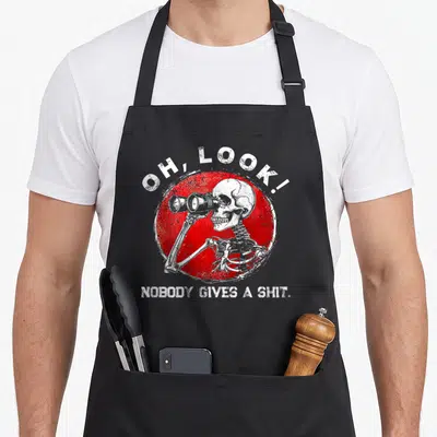 Nobody skeleton apron - Skeleton holding binoculars over red distressed circle with OH LOOK nobody gives a shit text — shown on a black cotton canvas apron against a white background