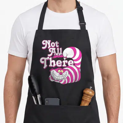 Funny cheshire alice wonderland apron - Pink and white striped cartoon cat with stacked text Not All There — shown on a black cotton canvas apron against a white background