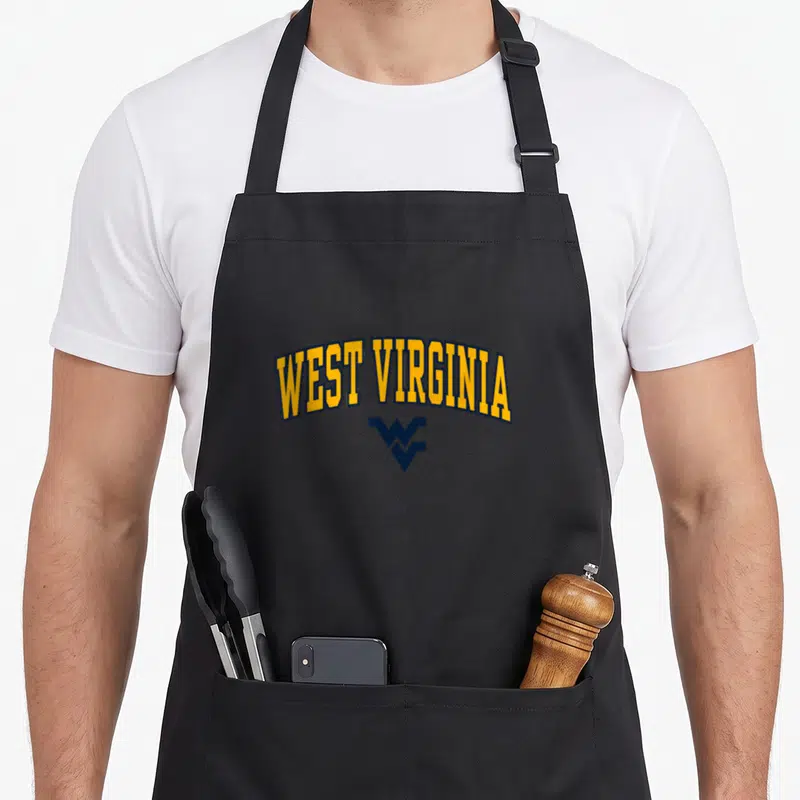 West arch apron - Arched yellow text reading WEST VIRGINIA above a navy blue interlocking WV monogram on a black — shown on a black cotton canvas apron against a white background