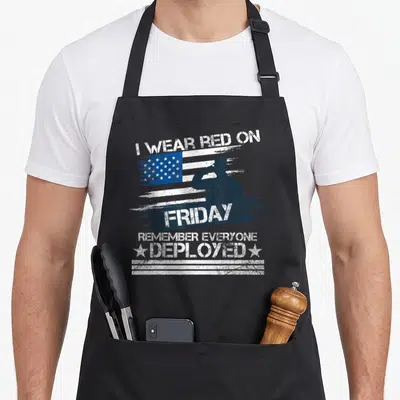 Friday military apron - Saluting soldier silhouette over distressed flag with text I wear red on Friday remember — shown on a black cotton canvas apron against a white background