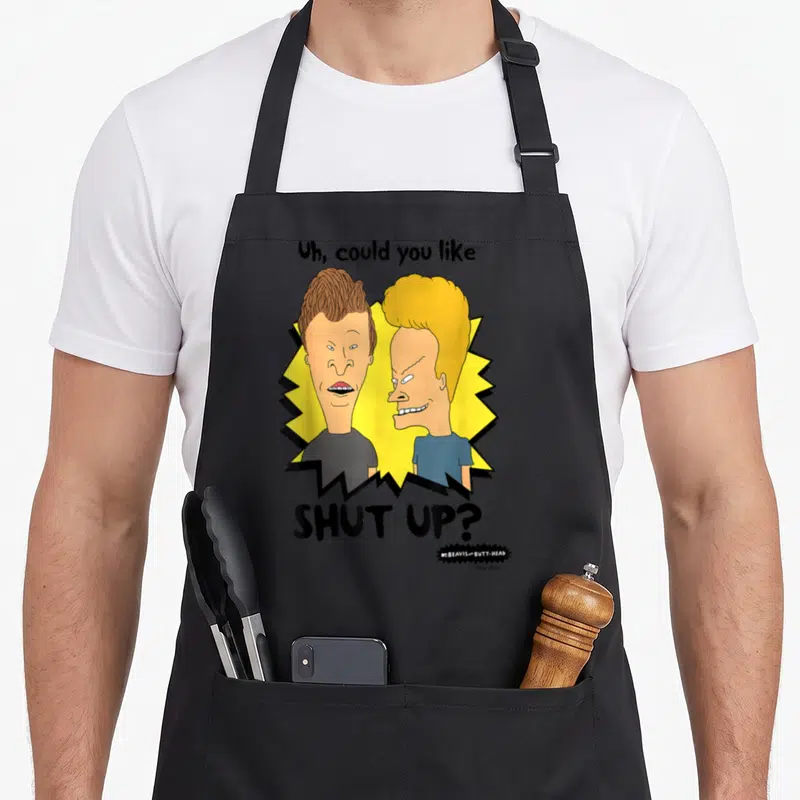 Butt judge apron - Beavis and Butt-Head cartoon faces on yellow burst with Shut Up text — shown on a black cotton canvas apron against a white background