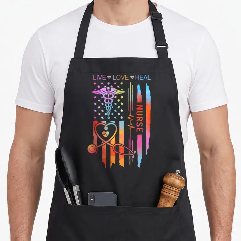 Appreciation nurse apron - Colorful caduceus and stethoscope heart over stars and stripes with LIVE LOVE HEAL text — shown on a black cotton canvas apron against a white background