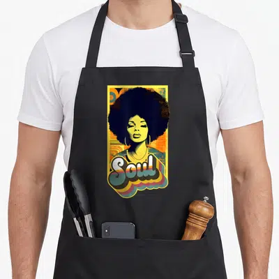 Vintage funk 70s apron - Stylized woman with large afro and Soul text in yellow, black, orange, and blue retro art — shown on a black cotton canvas apron against a white background