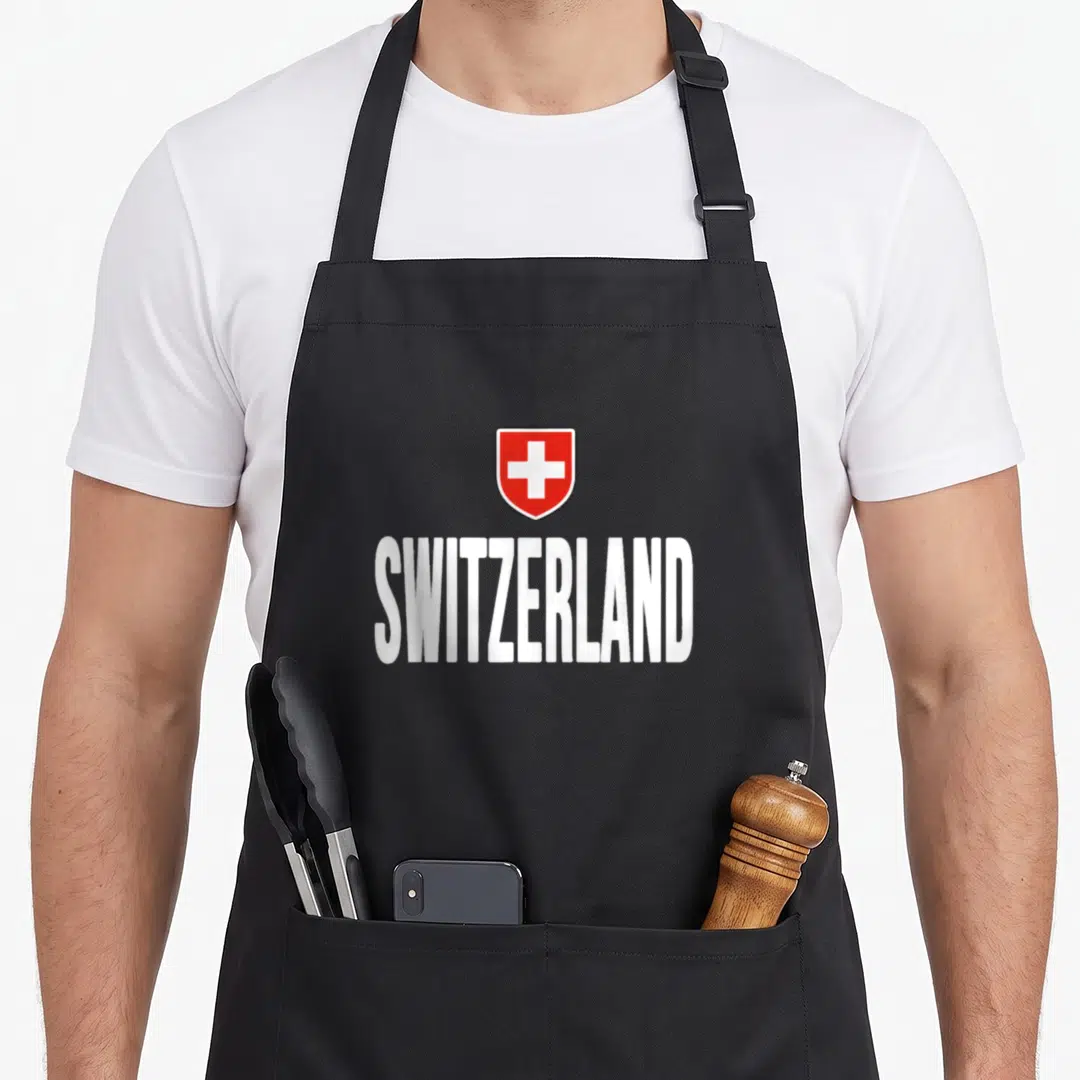 Schweiz swiss apron - Red shield with white cross above white SWITZERLAND text — shown on a black cotton canvas apron against a white background