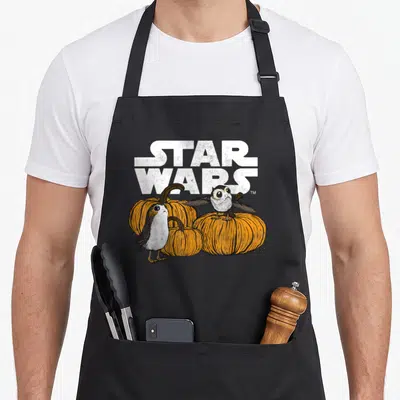 Porg halloween apron - Star Wars text above two porgs and three orange pumpkins in cartoon style — shown on a black cotton canvas apron against a white background