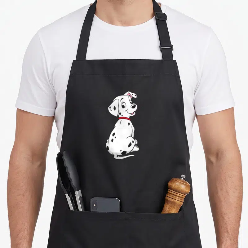 Rolly dalmatian apron - Cartoon white dalmatian puppy sitting with black spots and red collar — shown on a black cotton canvas apron against a white background