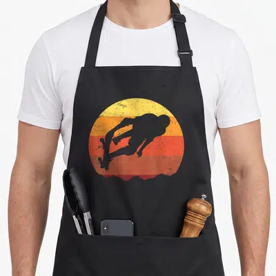 Skateboard skateboarding lover apron - Grey diver silhouette over yellow orange and red horizontal stripes in a retro — shown on a black cotton canvas apron against a white background