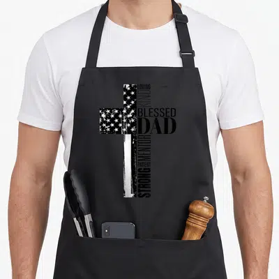 Christian blessed father day apron - Distressed cross formed by flag and text BLESSED DAD LOVING KIND MENTOR PATIENT — shown on a black cotton canvas apron against a white background