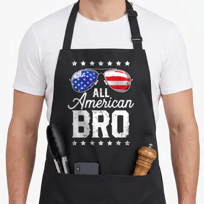 Bro 4th of july apron - Aviator sunglasses with US flag lenses above All American BRO text framed by white stars — shown on a black cotton canvas apron against a white background