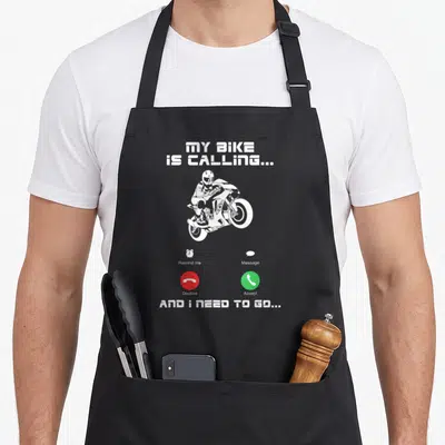 Calling motorcycle aprons - White motorcyclist with red and green phone interface icons and text MY BIKE IS CALLING — shown on a black cotton canvas apron against a white background