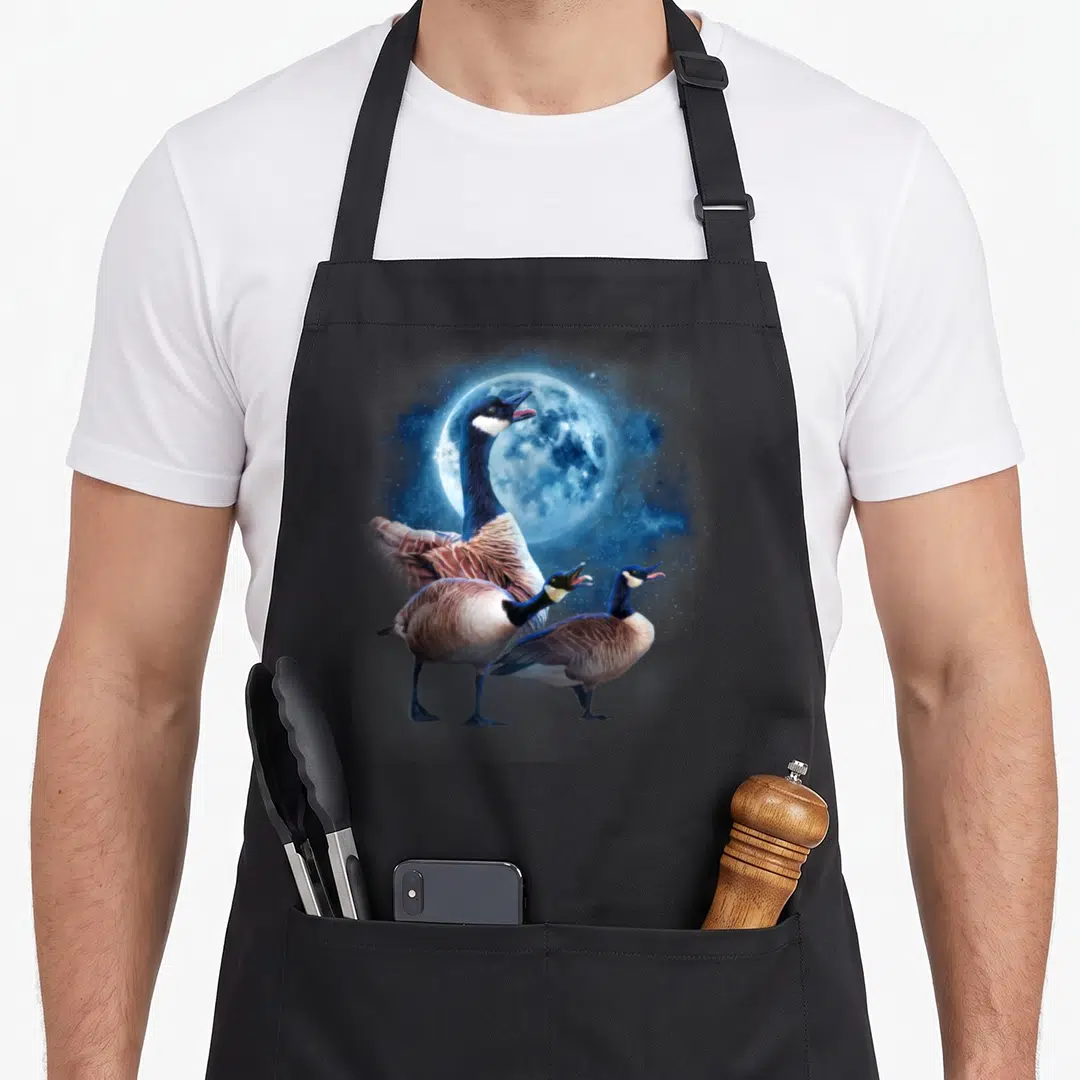 Howling silly apron - Three Canada geese standing under a large blue full moon with a starry sky background — shown on a black cotton canvas apron against a white background