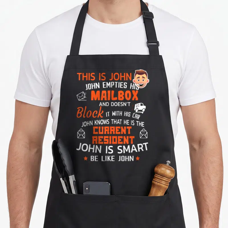 Carrier postal aprons - Orange and white text about John and a mailbox with cartoon man head and envelopes — shown on a black cotton canvas apron against a white background