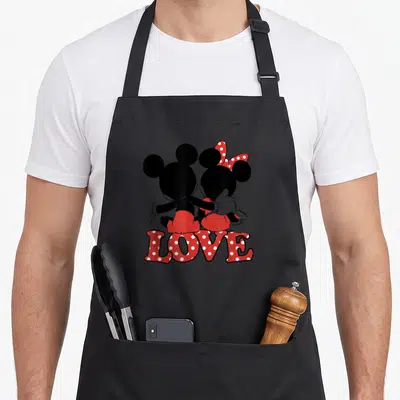 Hug valentine apron - Mickey and Minnie Mouse sitting back view with red polka dot LOVE text — shown on a black cotton canvas apron against a white background