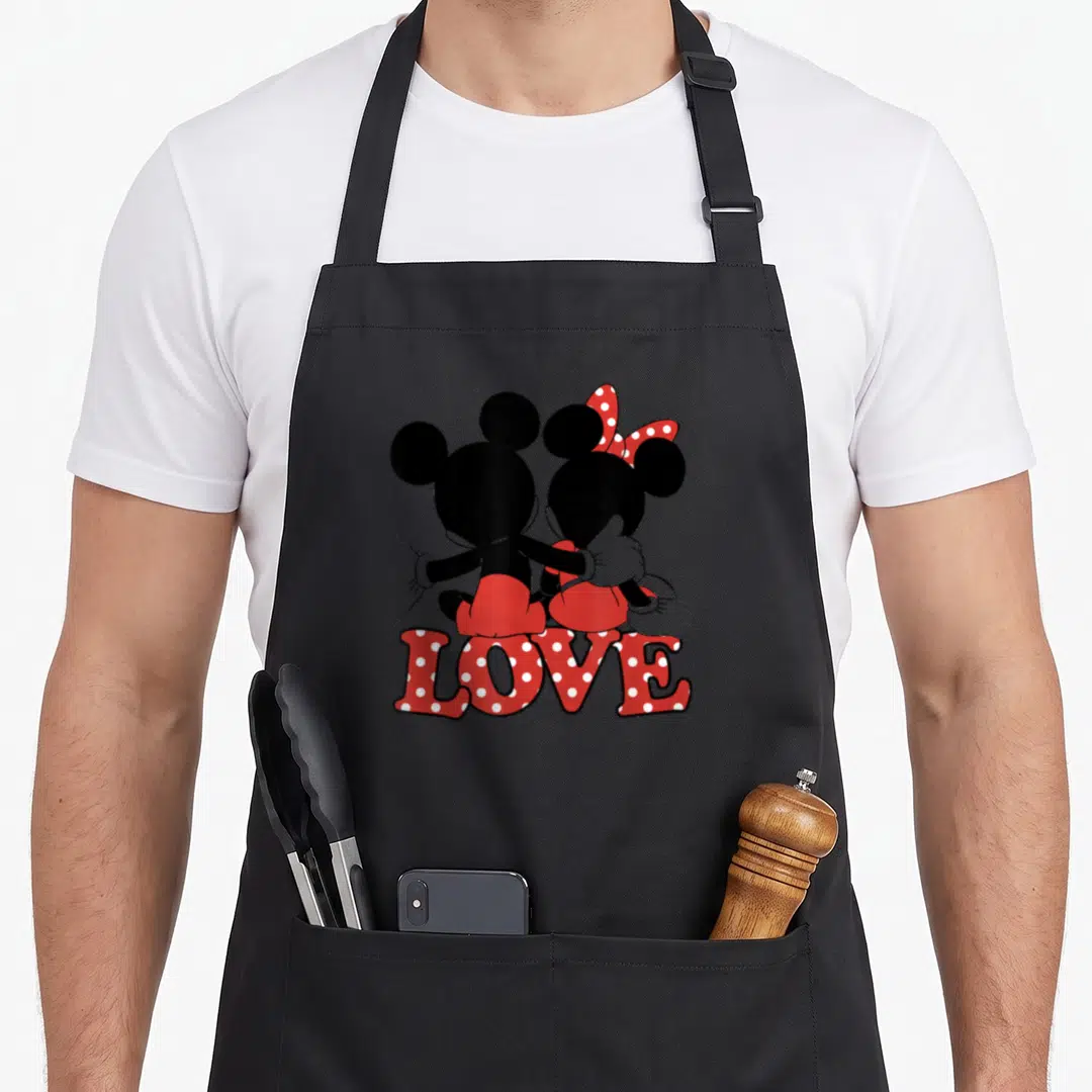 Hug valentine apron - Mickey and Minnie Mouse sitting back view with red polka dot LOVE text — shown on a black cotton canvas apron against a white background