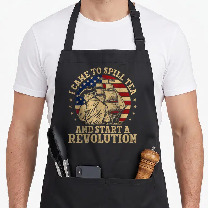 Flag tea party aprons - Distressed flag with man and ship and I CAME TO SPILL TEA text — shown on a black cotton canvas apron against a white background