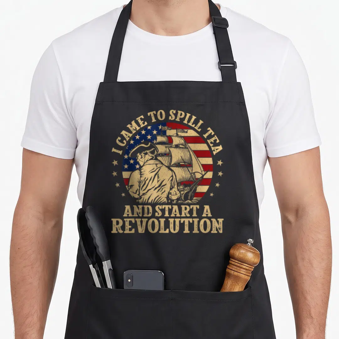 Flag tea party aprons - Distressed flag with man and ship and I CAME TO SPILL TEA text — shown on a black cotton canvas apron against a white background
