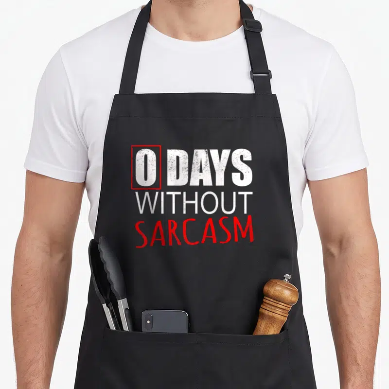 Funny sarcastic apron - Distressed white and red text reading 0 DAYS WITHOUT SARCASM with red rectangle around the zero — shown on a black cotton canvas apron against a white background
