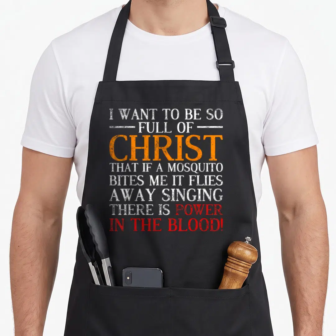Devotee christian apron - Stacked distressed text reading I want to be full of Christ mosquito bites power in the blood — shown on a black cotton canvas apron against a white background