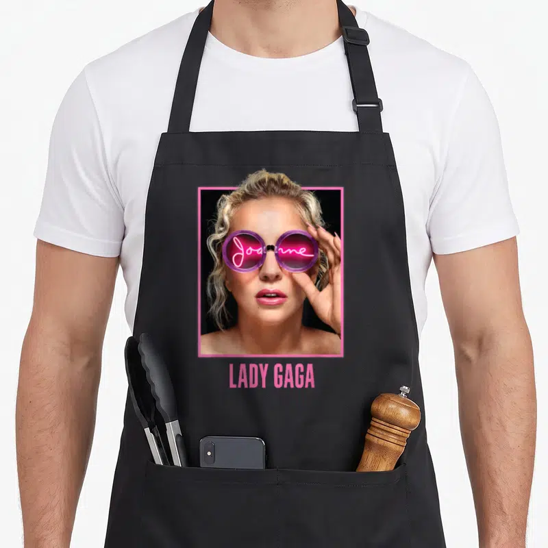 Gaga glass apron - Lady Gaga photo in pink frame, Joanne neon text in sunglasses, LADY GAGA below — shown on a black cotton canvas apron against a white background