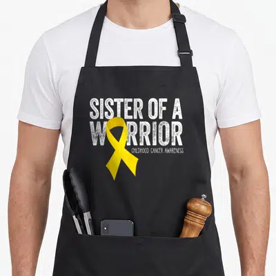 Sister ribbon apron - Yellow ribbon overlapping white distressed text reading Sister of a Warrior Childhood Cancer — shown on a black cotton canvas apron against a white background
