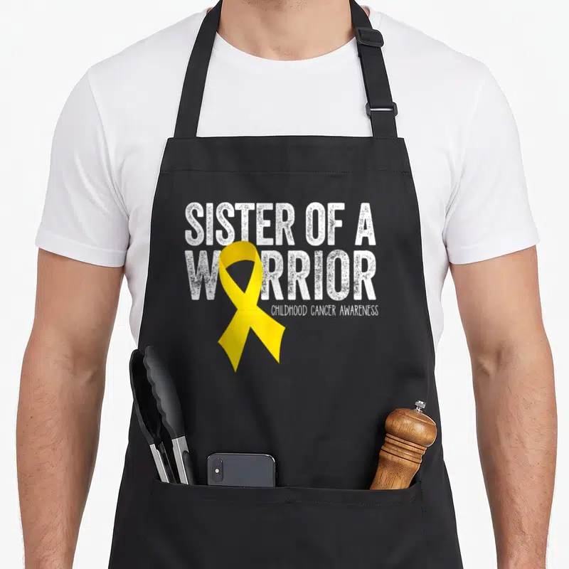 Sister ribbon apron - Yellow ribbon overlapping white distressed text reading Sister of a Warrior Childhood Cancer — shown on a black cotton canvas apron against a white background