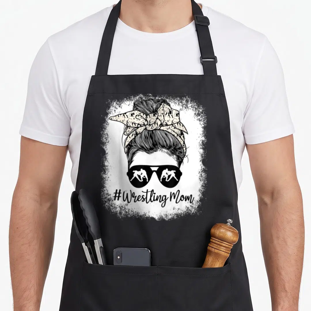 Wrestling messy aprons - #Wrestling Mom text under woman's head with sunglasses reflecting two wrestlers and messy bun — shown on a black cotton canvas apron against a white background