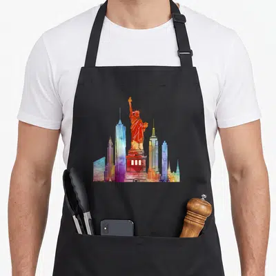 Watercolour new york apron - Statue of Liberty and skyscrapers in orange red blue purple yellow watercolor art — shown on a black cotton canvas apron against a white background