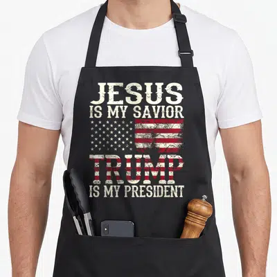 Jesus presidents apron - Distressed USA flag between JESUS IS MY SAVIOR and TRUMP IS MY PRESIDENT text in red white blue — shown on a black cotton canvas apron against a white background
