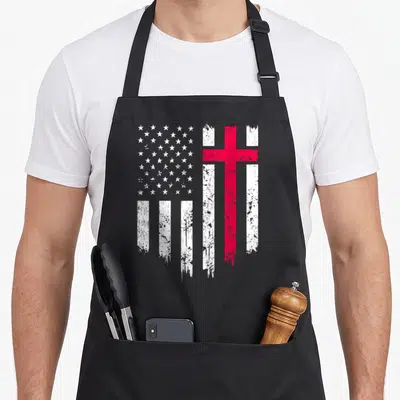 Distressed funny christian aprons - Distressed US flag design with white stars and red cross stripes on black fabric — shown on a black cotton canvas apron against a white background