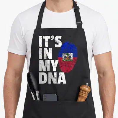 Dna country apron - Distressed IT'S IN MY DNA text next to blue red fingerprint containing Haitian flag — shown on a black cotton canvas apron against a white background