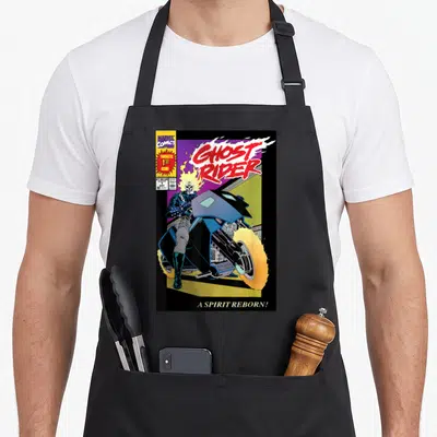 Number ghost apron - Ghost Rider comic cover print with flaming skull, motorcycle, and caption A Spirit Reborn — shown on a black cotton canvas apron against a white background