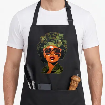 Camouflage african american aprons - Cartoon woman portrait with orange skin, sunglasses, and green brown camo hair — shown on a black cotton canvas apron against a white background