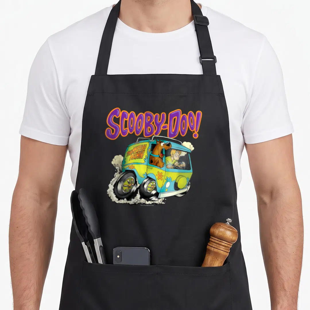 Scoob decade apron - SCOOBY-DOO! text above Mystery Machine van with characters and smoke clouds — shown on a black cotton canvas apron against a white background
