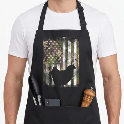 Patriotic farmers apron - Grey chicken silhouette over distressed green brown tan white grey camouflage USA flag pattern — shown on a black cotton canvas apron against a white background