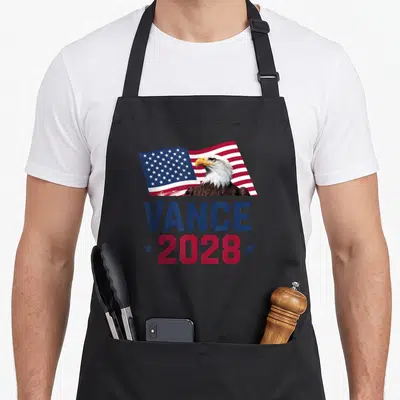 President jd apron - Bald eagle in front of waving USA flag with VANCE 2028 text in blue and red — shown on a black cotton canvas apron against a white background