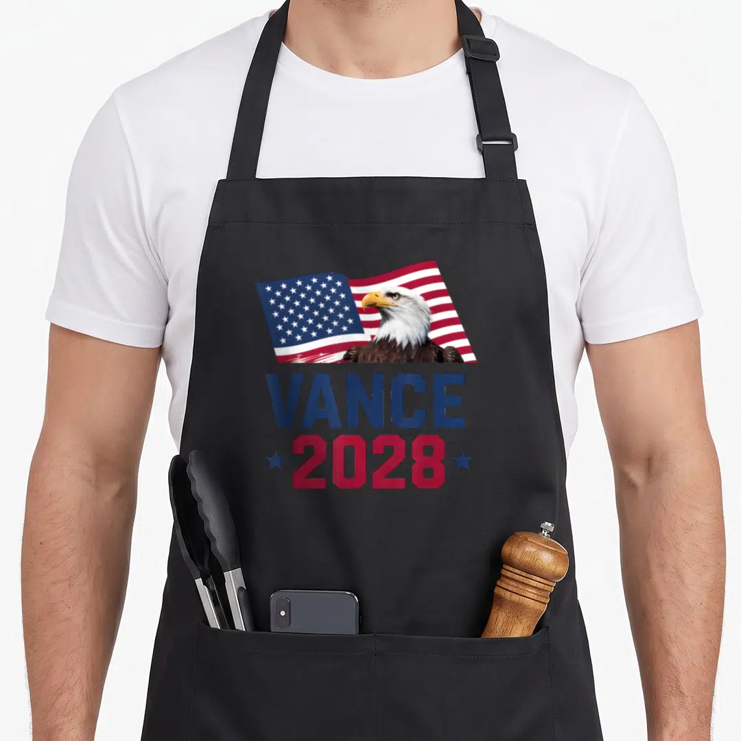 President jd apron - Bald eagle in front of waving USA flag with VANCE 2028 text in blue and red — shown on a black cotton canvas apron against a white background