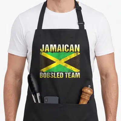 Jamaican jamaica bobsled apron - Distressed Jamaican flag centered between JAMAICAN and BOBSLED TEAM text in yellow — shown on a black cotton canvas apron against a white background