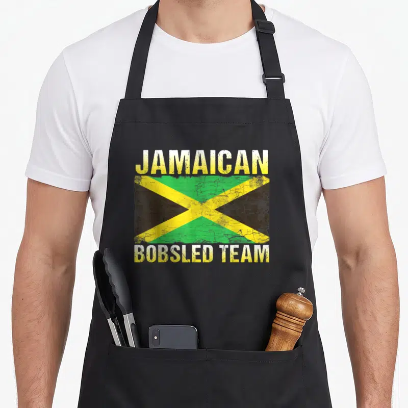 Jamaican jamaica bobsled apron - Distressed Jamaican flag centered between JAMAICAN and BOBSLED TEAM text in yellow — shown on a black cotton canvas apron against a white background