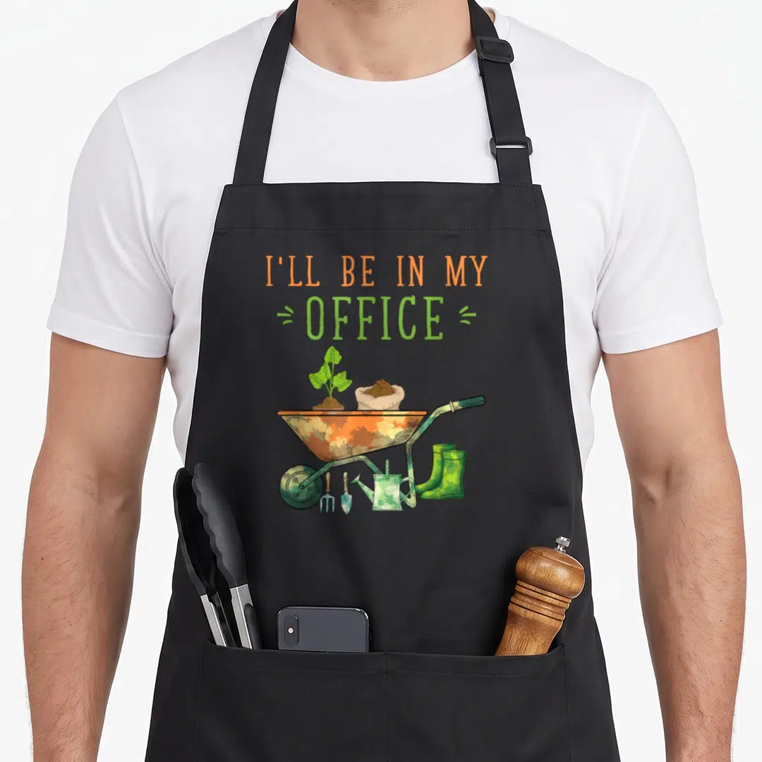 Landscaper gardening gardener apron - I'll be in my office text above cartoon wheelbarrow with plant, soil, boots — shown on a black cotton canvas apron against a white background