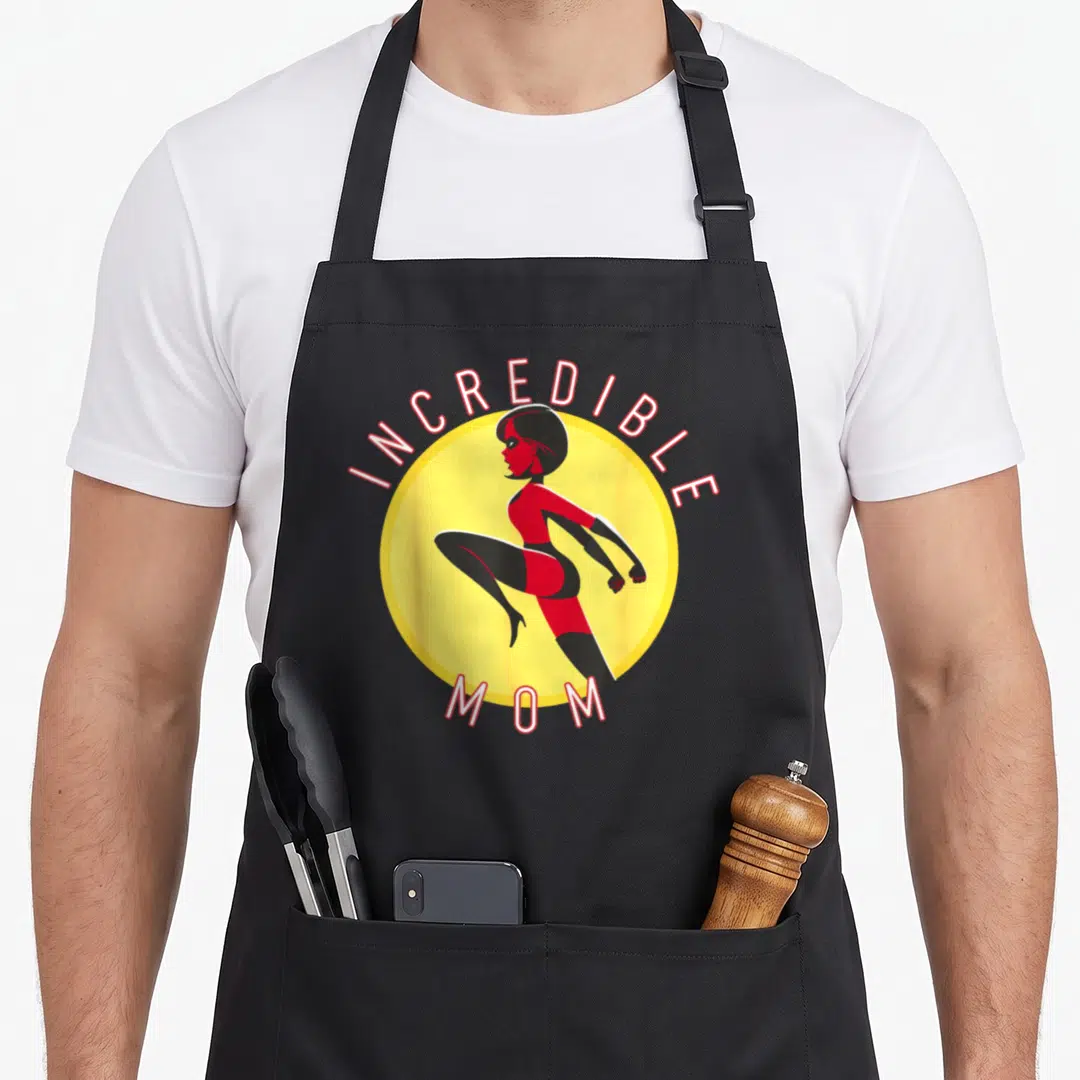 Incredible wife mom apron - Woman in red suit inside yellow circle with INCREDIBLE MOM text arched around it — shown on a black cotton canvas apron against a white background