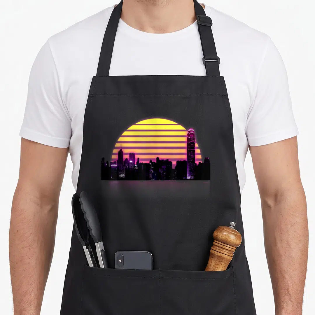 Synthwave retrowave 80s apron - Purple city skyline silhouette against a striped yellow and orange sun in retro style — shown on a black cotton canvas apron against a white background