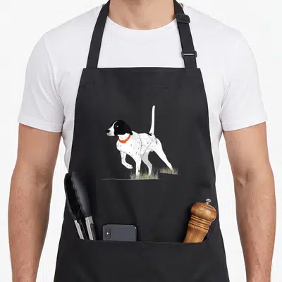 Bird pointer apron - Cartoon black and white spotted dog with orange collar standing in grass — shown on a black cotton canvas apron against a white background