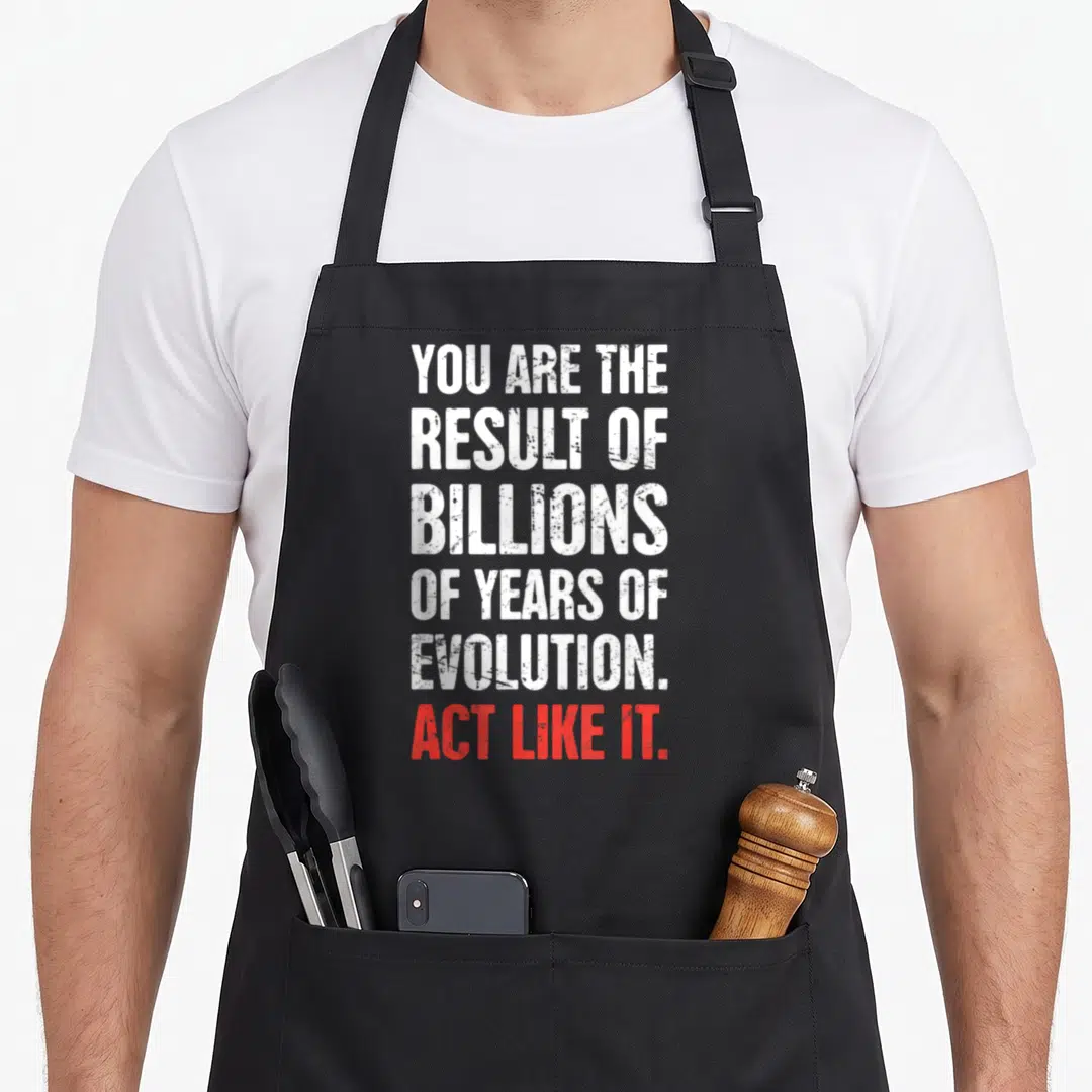 Atheism charles apron - Stacked white and red text reading YOU ARE THE RESULT OF BILLIONS OF YEARS OF EVOLUTION ACT — shown on a black cotton canvas apron against a white background