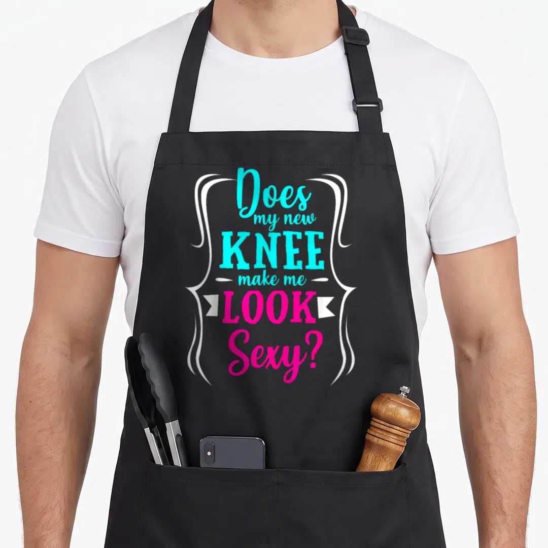 Knee recovery day apron - Cyan and pink stacked text reading Does my new knee make me look sexy inside white brackets — shown on a black cotton canvas apron against a white background